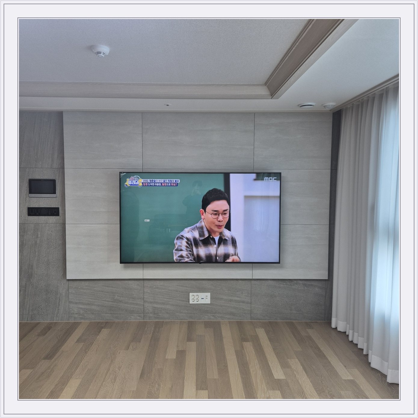 거실 회색 패널과 벽걸이 TV, TV 아래 콘센트와 양쪽 마감 판넬의 대비가 뚜렷합니다