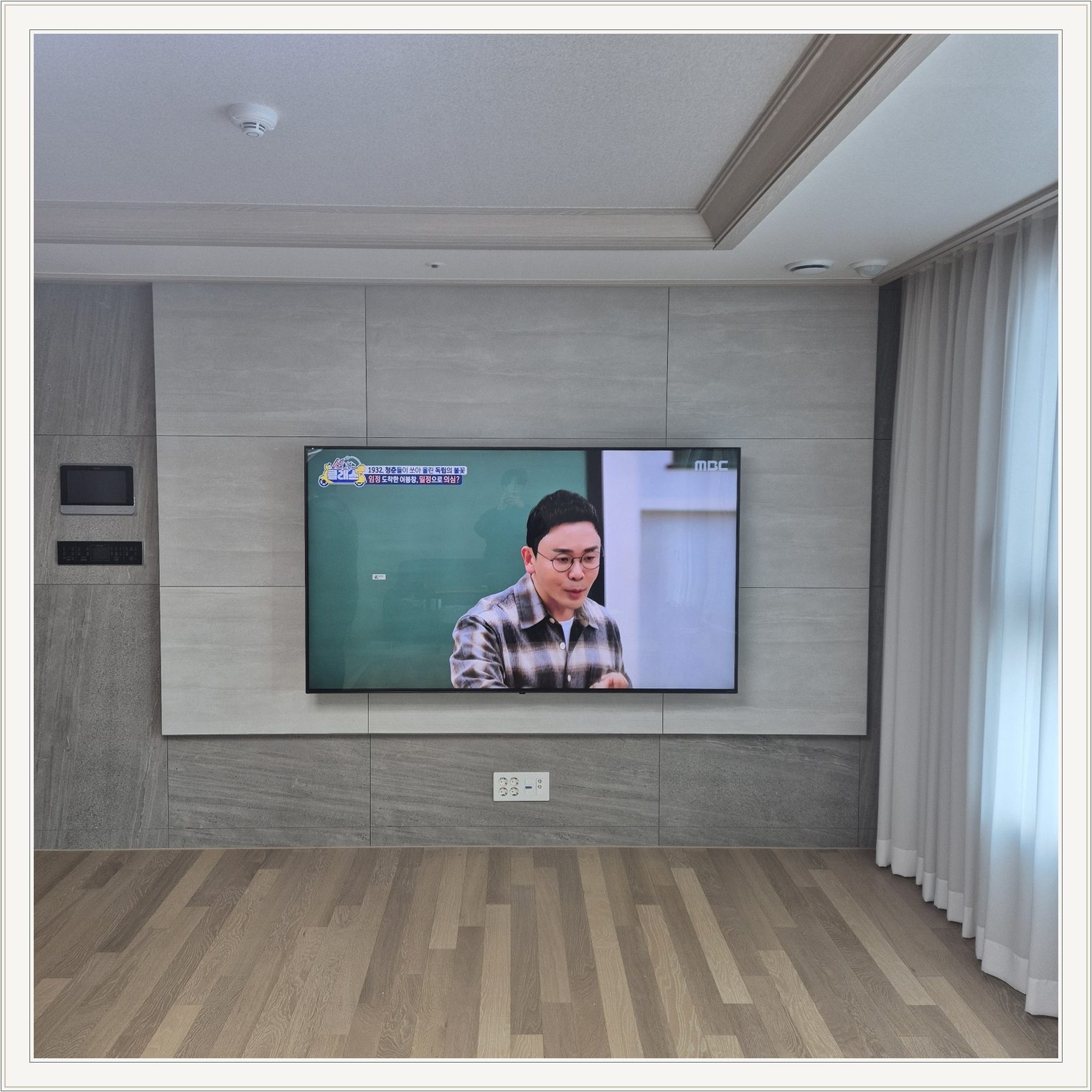 거실 회색 패널과 벽걸이 TV, TV 아래 콘센트와 양쪽 마감 판넬의 대비가 뚜렷합니다